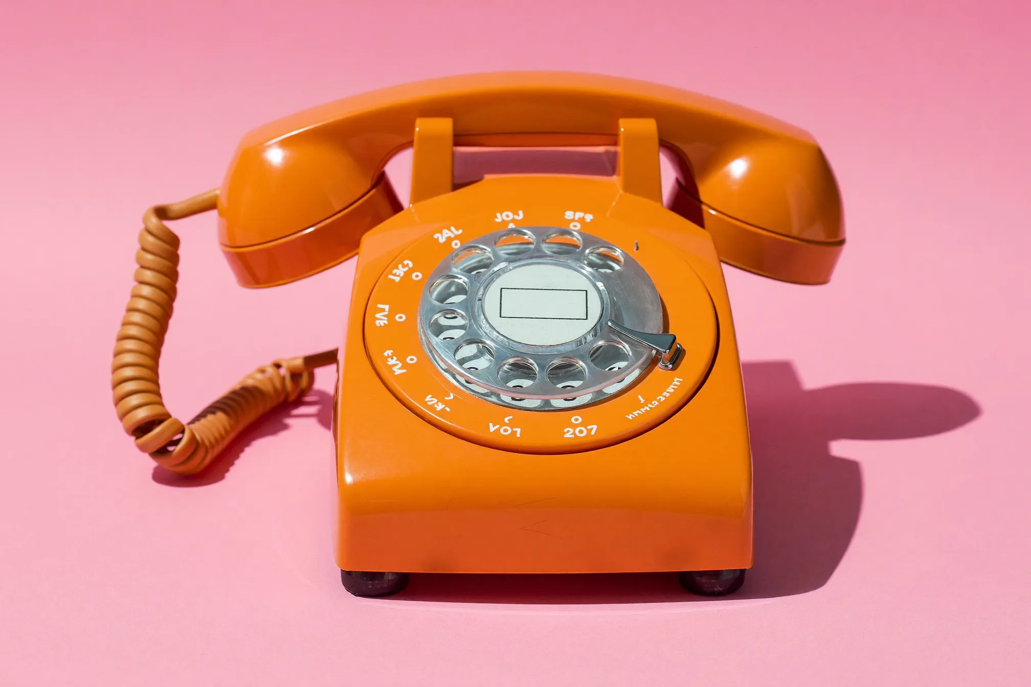 Orange rotary phone on a pink background